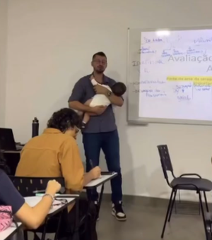 Professor segura bebê de aluna no colo durante a aula para ajudar aluna