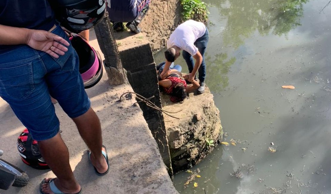 Mulher cai em riacho poluído e homem pula para ajudar, em Arapiraca