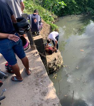 Mulher cai em riacho poluído e homem pula para ajudar, em Arapiraca