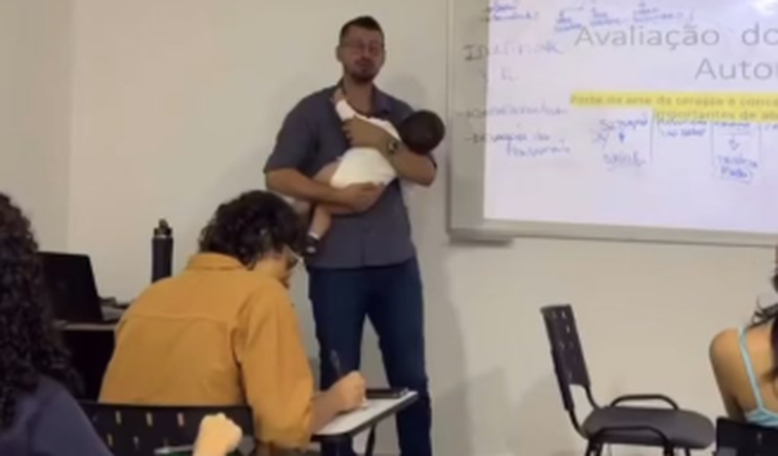Professor segura bebê de aluna no colo durante a aula para ajudar aluna