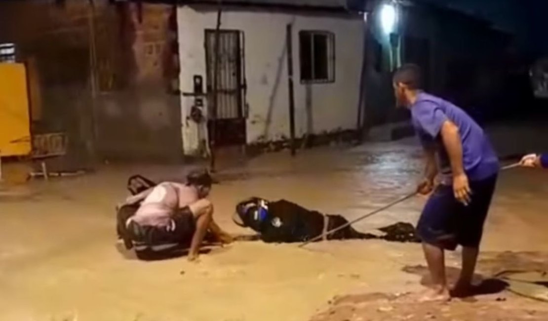Motociclista tenta atravessar rua alagada e fica preso em buraco no Jacintinho